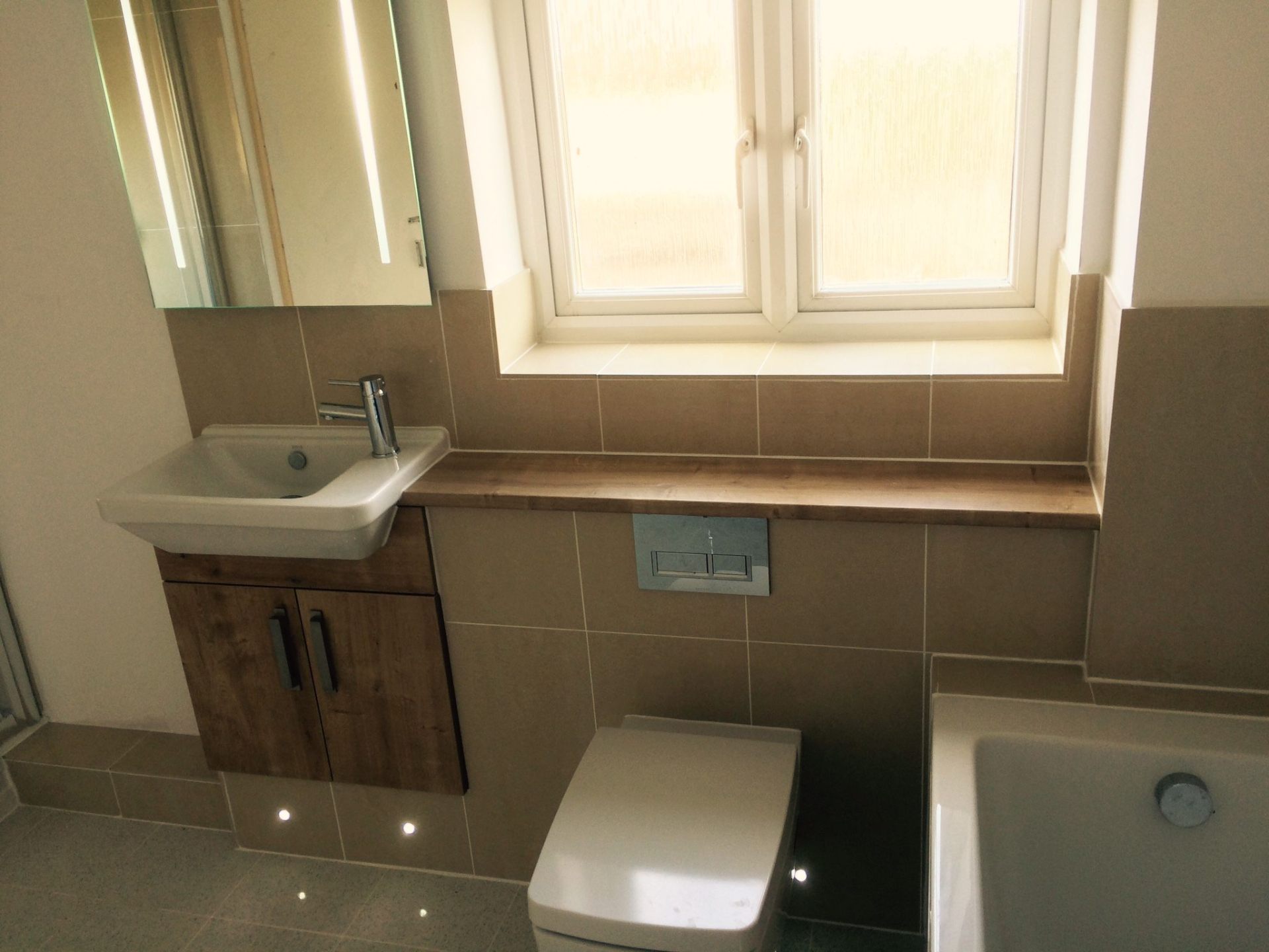 Compact fitted bathroom with wood-effect vanity, WC and natural light from side window