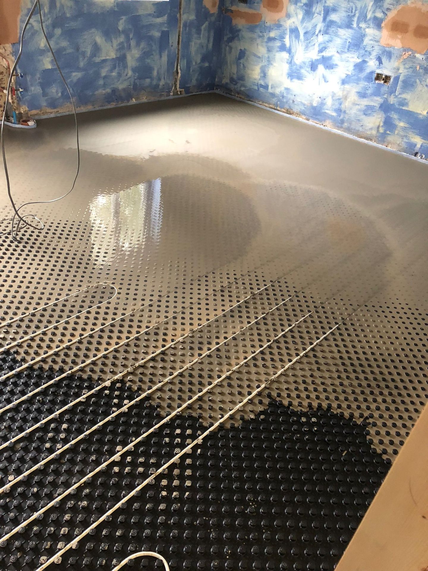 Wet underfloor heating pipes on dimple insulation board being covered with liquid screed