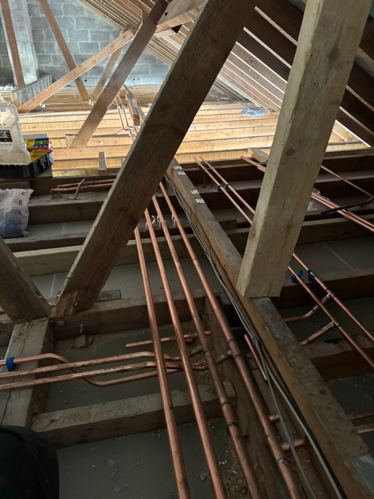 Wet underfloor heating pipe loops laid in aluminium spreader plates between floor joists during a plumbing first-fix