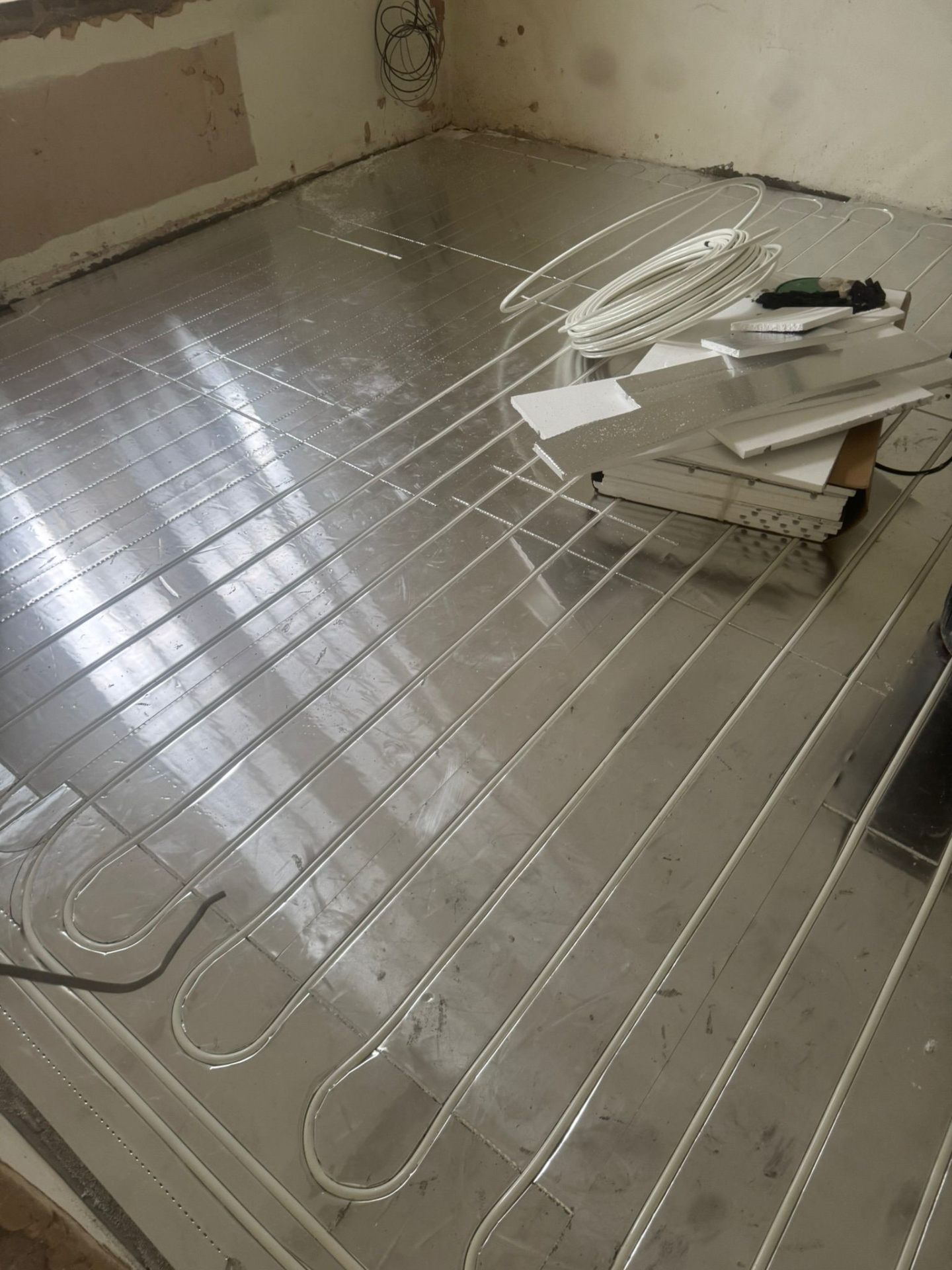 Wet underfloor heating pipe circuits laid across foil-backed insulation panels ready for screed