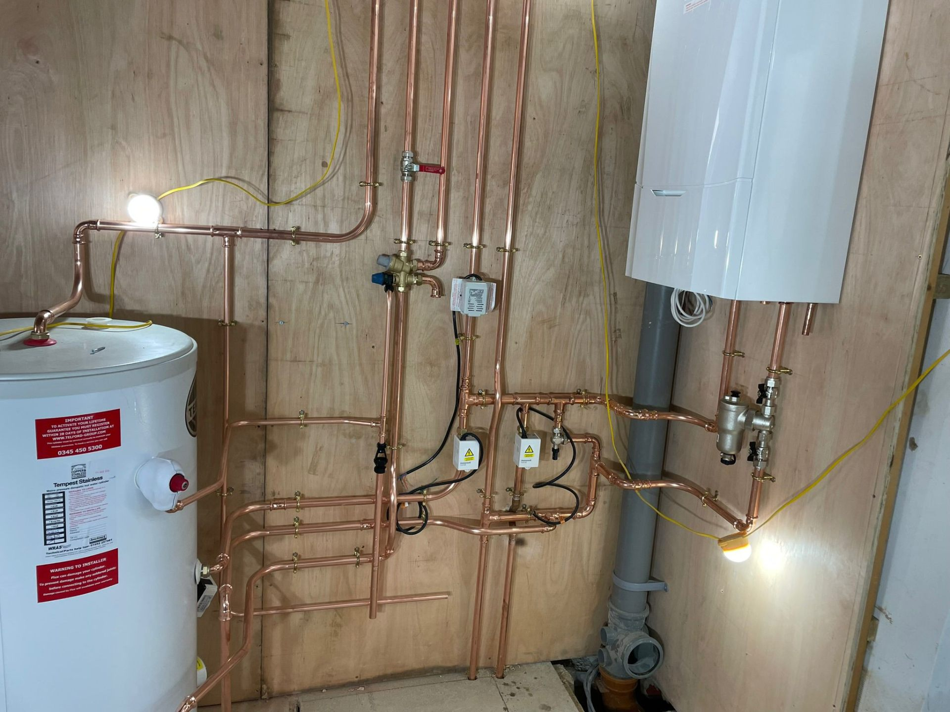 Detailed copper pipework, cylinder and wall-hung gas boiler mid-repair with system filter and motorised valves